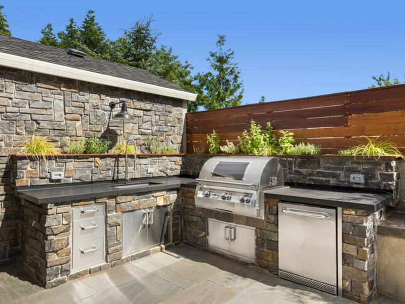 stone outdoor kitchen with a grill and fridge